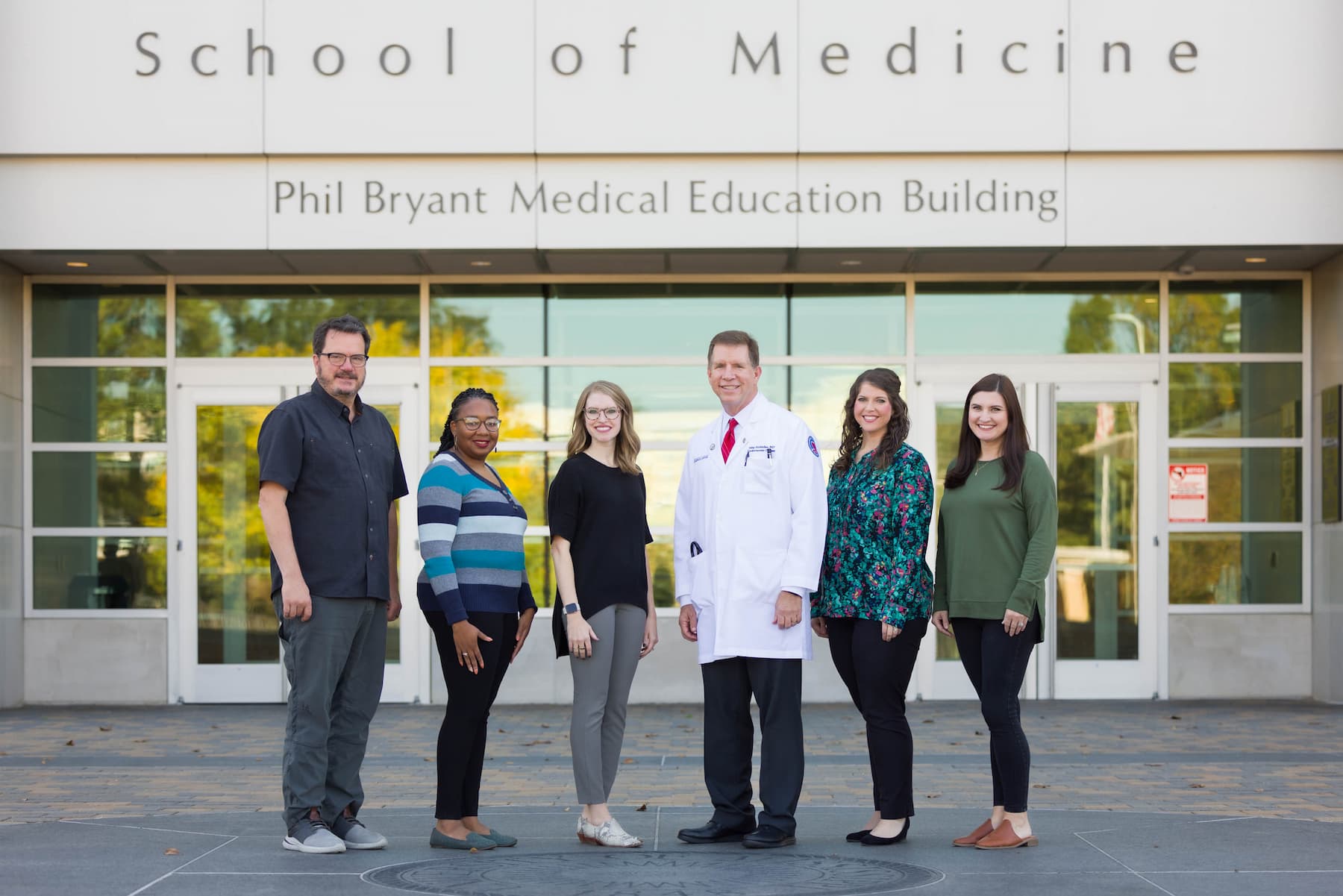 Six members of the SOM Student Affairs Team standing in front of the School of Medicine. From left to right: Dr. Jerry Clark, Jessica Nickols, Dr. Lyssa Weatherly, Dr. Michael McMullan, Tressie Nichols, Felicity Broderick.